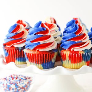 pinterest image for red, white and blue cupcakes - cupcakes on a white cake stand and one with a bite out