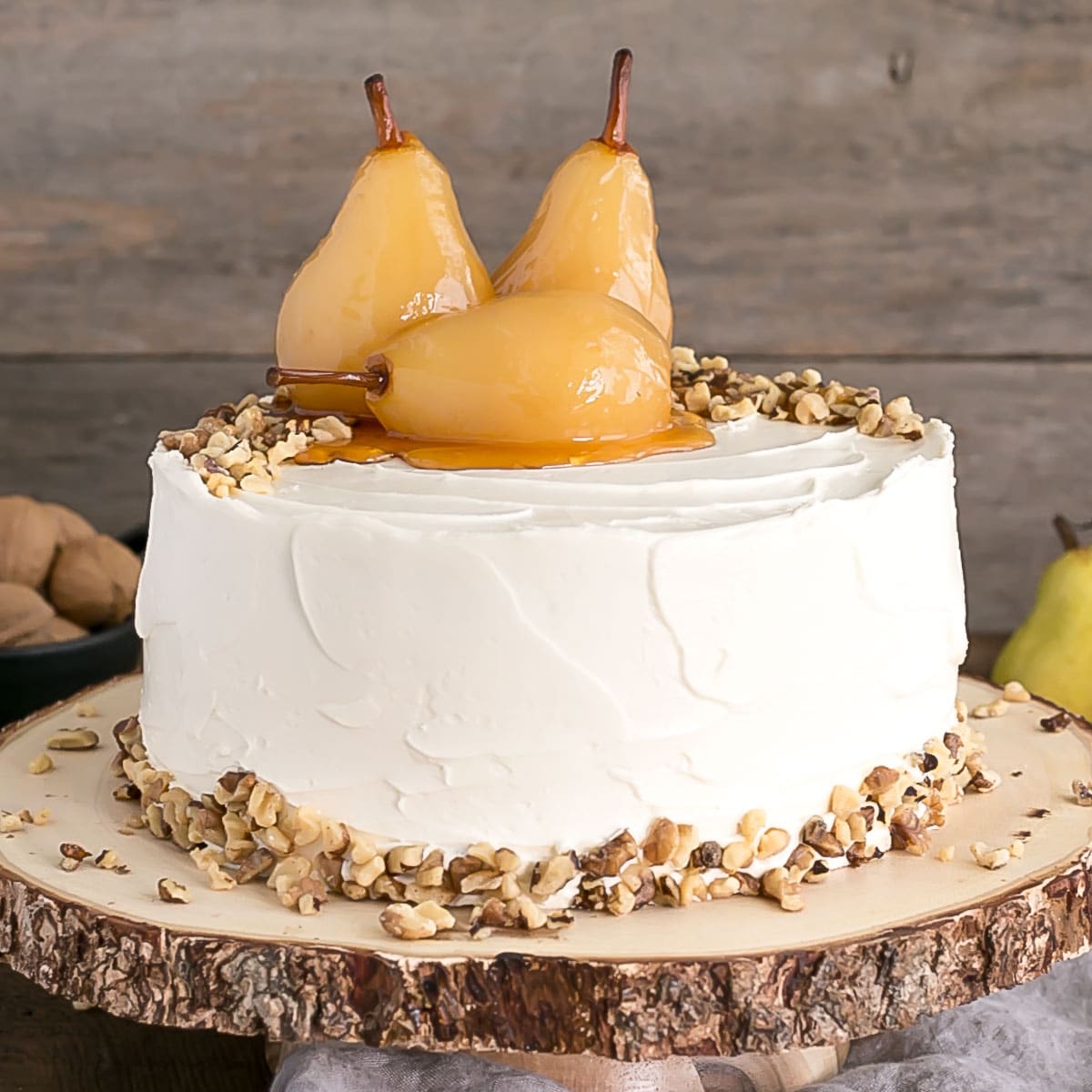 Walnut cake with poached pears on top on a rustic wooden cake stand.